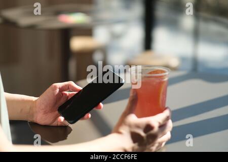 close up man's hand using smart phone in cafe, with a cup of cold drink on table Stock Photo