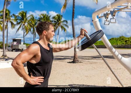 Outdoor Gym - Fitness man working out biceps muscles at outdoor public calisthenic gym on South Beach doing T-bar barbell extensions training on South Stock Photo