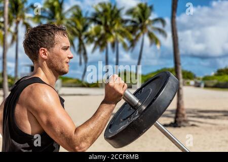 Outdoor calisthenics gym park male athlete working out on T-bar outside in summer. Man workout strength training arms biceps muscles with heavy Stock Photo