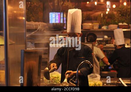 Cambodian New Year was re-scheduled this year due to a fear of an outbreak of coronavirus. during the re-scheduled event, a Cambodian chef, wearing a chef's hat & protective face mask / covering, is cooking at an open-air Khmer BBQ restaurant near Pub Street during the COVID - 19 pandemic. Siem Reap, Cambodia. August 21st, 2020. © Kraig Lieb Stock Photo