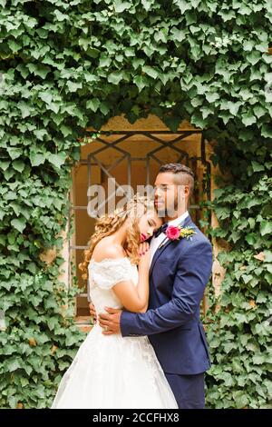 Wedding, newlyweds, young adults, diversity, portrait garden, window, hug Stock Photo