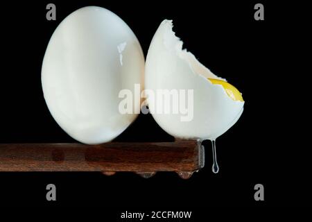 Chicken eggs, one egg is broken in which the yolk is visible and the white flows down on a black background. Close up Stock Photo