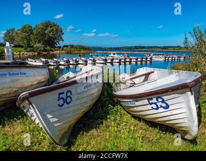 Numbered boats on land, with a line of motor boats behind on Rutland Water – a reservoir, artificial lake and nature reserve in Rutland, England, UK. Stock Photo
