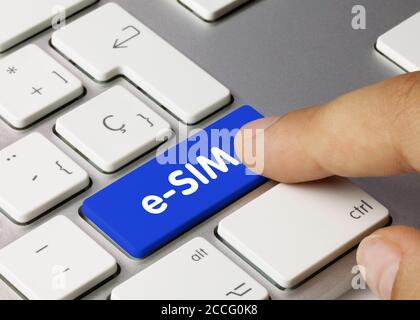eSIM Written on Blue Key of Metallic Keyboard. Finger pressing key. Stock Photo