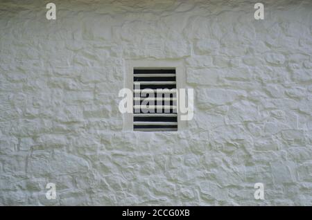 Old slatted ventilation window in a whitewashed stone wall on historic farm. Full frame rustic image in natural light with copy space. Stock Photo