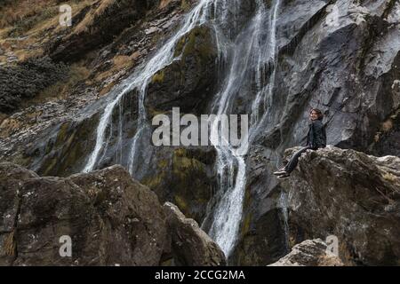 Girl sitting on a rock near waterfall. Powerscourt Waterfall, Wicklow Mountains, Ireland. Stock Photo