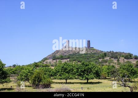Ruines of hazmburk castle on top of mountain peak of ceske stredohori range. Fruit trees and blue sky. Stock Photo