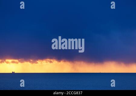 Europe, Germany, Lower Saxony, Otterndorf. Under heavy, dark rain clouds, a single freighter sails across the mouth of the Elbe. Stock Photo