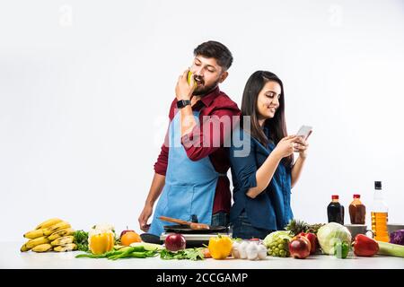 Indian couple in kitchen - Young Beautiful asian wife enjoying cooking with husband with lots of fresh vegetables and fruits Stock Photo