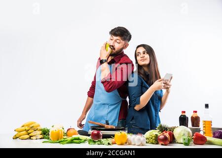 Indian couple in kitchen - Young Beautiful asian wife enjoying cooking with husband with lots of fresh vegetables and fruits Stock Photo