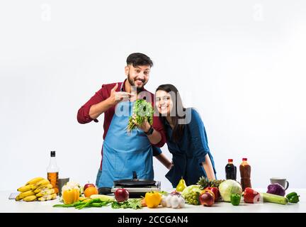 Indian couple in kitchen - Young Beautiful asian wife enjoying cooking with husband with lots of fresh vegetables and fruits Stock Photo