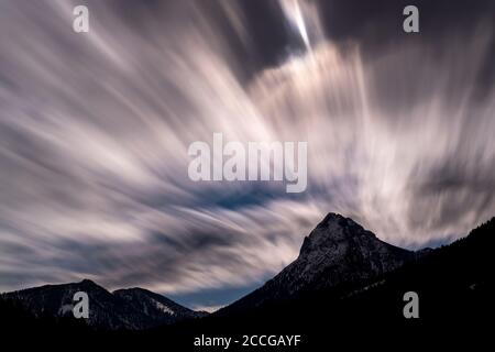 Long exposure during a cold winter night of the fast moving clouds over the Guffert in Rofan under a full moon. The moonlight illuminates the clouds f Stock Photo