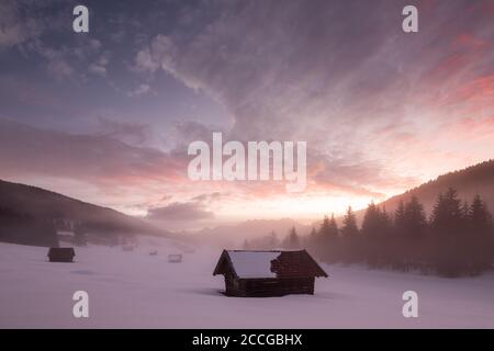 Haystack in the snow at sunrise in the Werdenfelser Land near Garmisch-Partenkirchen. In the background the Soierngruppe, in the foreground the pebble Stock Photo