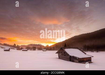 Dawn in the Werdenfelser Land. Some haystacks stand in the fresh snow, while in the background the Sowendgruppe of the Karwendel emphasizes the landsc Stock Photo