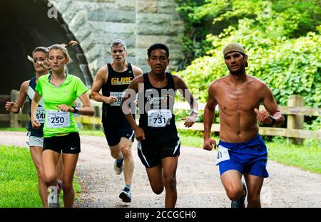 Babylon, New York, USA - 12 August 2018: Fast runners emerging from under the tunnel during the Dirty Sock 10K trail race. Stock Photo