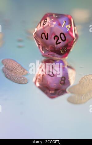 Close up of a pink transparent d20 dice on a wet reflective pastel colered surface with foam Stock Photo