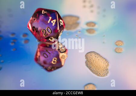 Close up of a pink polyhedral dice on a blue reflecting surface with soap foam Stock Photo