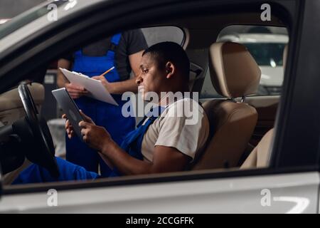 Workers in blue overalls inspect the car inside and use the tablet Stock Photo