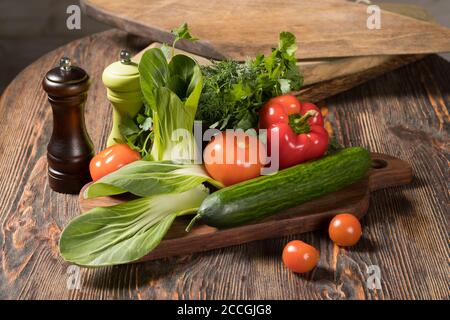 Fresh vegetables tomatoes, cucumber, sweet bell pepper, fresh herbs, parsley, dill, salad lie on a wooden table Stock Photo