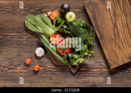 Fresh vegetables tomatoes, cucumber, sweet bell pepper, garlic, fresh herbs, parsley, dill, salad lie on a wooden table Stock Photo