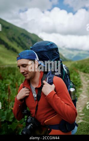 Young tourist man walking by the mountain road with big backpack. Photographer backpacker traveling in the mountains with his camera. Stock Photo