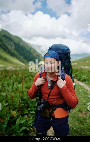 Young tourist man walking by the mountain road with big backpack. Photographer backpacker traveling in the mountains with his camera. Stock Photo