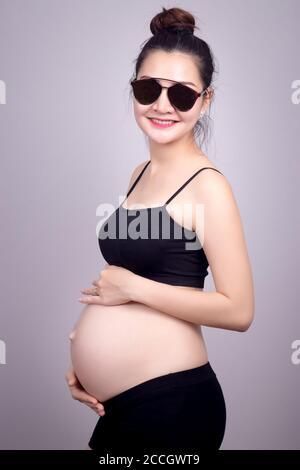 Happy mom concept : Portrait of happy pregnant Asian woman with smile face in black dress with sun glasses. Beautiful Asia female model in her 20s.