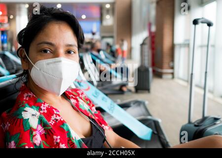 Barcelona, Spain - 20 august 2020: a young woman sit inside airport with face mask, looking in camera, going on holidays during a coronavirus global p Stock Photo