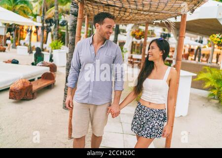 Summer vacation happy couple at tropical beach resort hotel walking to the beach. Young interracial people holding hands in casual clothes. Caribbean Stock Photo