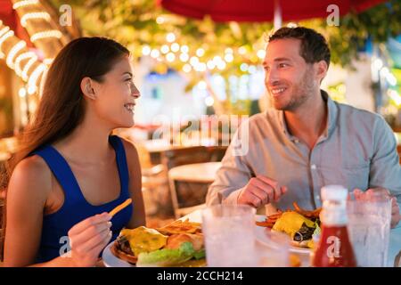 Couple eating hamburgers at outdoor restaurant terrace happy tourists on summer vacation. Florida travel people eating food at night during holidays Stock Photo