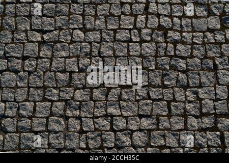 Top view of many irregular  rough square stone paving blocks with brown sand jointing Stock Photo