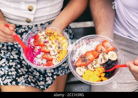 Acai bowl and pitaya dragonfruit smoothie healthy breakfast bowls young friends eating together. Couple man and woman eating sitting outside in park Stock Photo