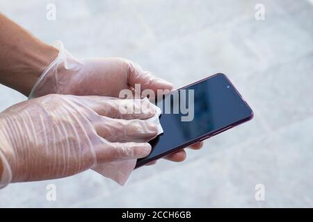 Hands with disposable gloves on, wiping smartphone screen with a white cloth. Stock Photo