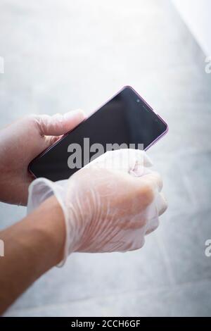 Hands with disposable gloves on, wiping smartphone screen with a white cloth. Vertical shot. Stock Photo