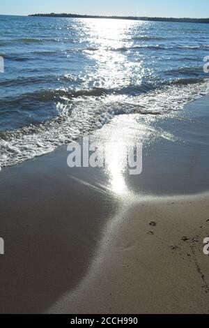 Beach on Lake Huron with sunlit waves and footprints Stock Photo