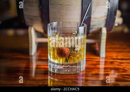 A classic craft cocktail made with bourbon whiskey sits in front of a barrel on a wooden bar. Stock Photo