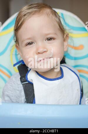 Cute baby child portrait getting messy eating cereals or porridge by itself. Stock Photo