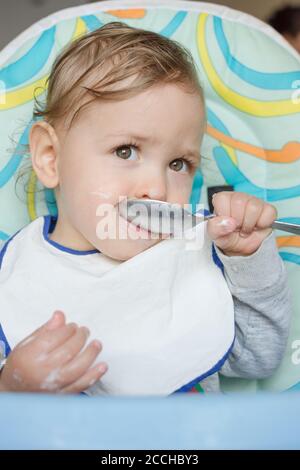 Cute baby child portrait getting messy eating cereals or porridge by itself. Stock Photo