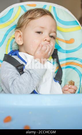 Cute baby child getting messy eating by itself. Stock Photo