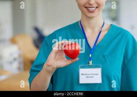 Close-up of female cardio doctor in uniform holding heart shape and smiling while standing at hospital Stock Photo