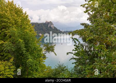 Iconic Slovenian landscape, with a distant castle nestled on a promotory overlooking the lake Bled, framed by green vegetation