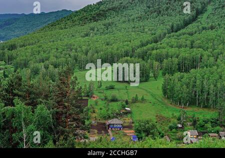 Russian rural landscape in summer, village houses in greenery. The nature of Khakassia, the Sayan Mountains under a cloudy sky. Stock Photo