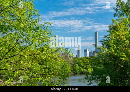 Midtown Manhattan skyscraper stands behind fresh green trees in the Central Park Stock Photo