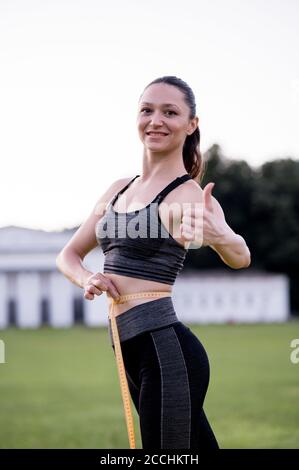 Beautiful young woman, while wearing a tight sports outfit, measures her waist after doing pilates or yoga exercises Stock Photo