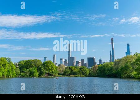 Midtown Manhattan skyscraper stands behind fresh green trees in the Central Park Stock Photo