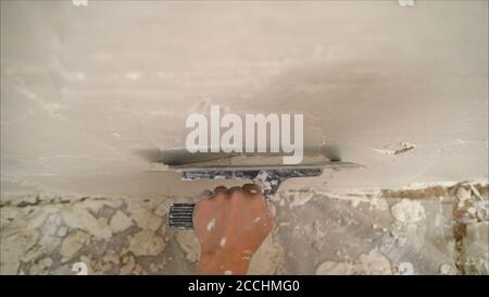construction notched trowel and worker hands with white mortar on wall. Worker levels a wall with mortar Stock Photo