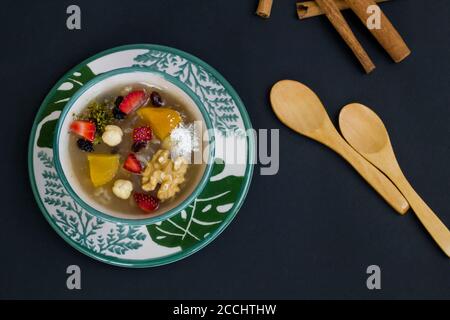 Traditional Turkish Dessert Noah's Puding in stylish green bowl on black surface with spoon and copy space.Top view. Stock Photo