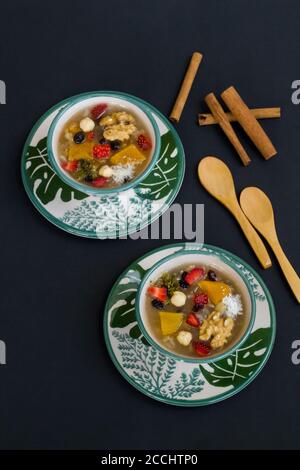 Traditional Turkish Dessert Noah's Puding in stylish green bowl on black surface with spoon and copy space.Top view. Stock Photo