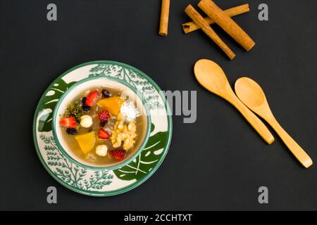 Traditional Turkish Dessert Noah's Puding in stylish green bowl on black surface with spoon and copy space.Top view. Stock Photo