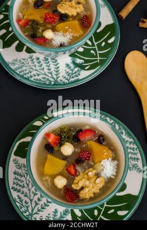 Traditional Turkish Dessert Noah's Puding in stylish green bowl on black surface with spoon and copy space.Top view. Stock Photo